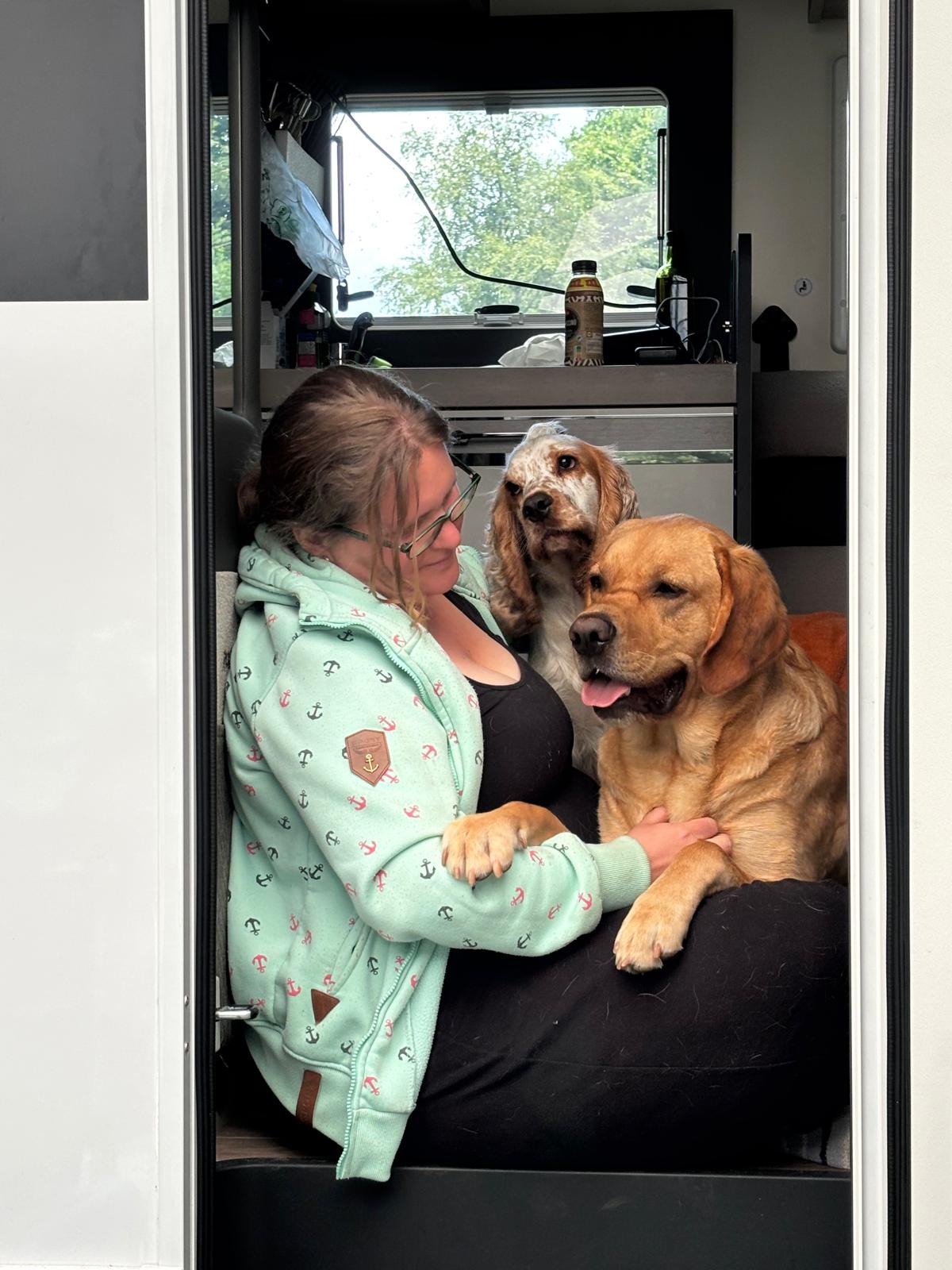 Merle mit Muffin und Fiete Ruhrpawt Blonde Frau im Profil mit einem Labrador Mischling auf dem Schoss und einem Cocker Spaniel im Hintergrund, der sie anschaut